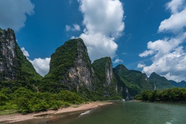Çin 'in Guilin ve Yangshuo kasabaları arasında akan görkemli Li nehri üzerinde karst dağlarının yüksek dikey uçurumlarında seyahat eden turistleri taşıyan bir tekne.