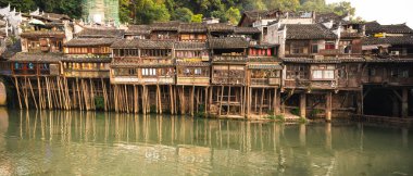 Feng Huang, China -  August 2019 : Panoramic view of the old historic wooden Diaojiao houses on the riverbanks of Tuo river, flowing through the centre of Fenghuang Old Town clipart