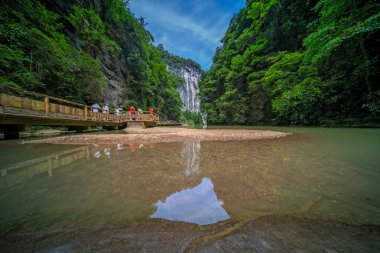 Turistler, Wulong bölgesi, Chongqing, Çin 'deki Longshuixia Fissure Ulusal Parkı' ndaki devasa dikey kaya duvarları boyunca akan nehir boyunca tahta bir köprü üzerinde yürüyorlar.