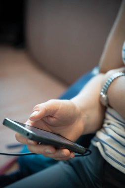 Havaalanı salonunda oturan, elinde tutan ve e-posta göndermek ve almak için akıllı telefon kullanan bir kadın.