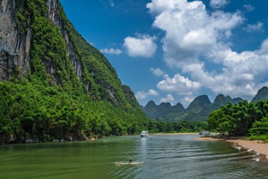 Yaşlı balıkçı, Guilin ve Yangshuo kasabaları arasındaki görkemli Li nehrinin çarpıcı karst dağ manzarasının arasında küçük tahta bir teknede kürek çekiyor.