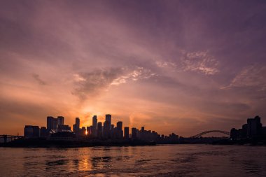 Çin 'in Chongqing şehrinde gün batımında deniz altında çevrili binaların siluetleri.
