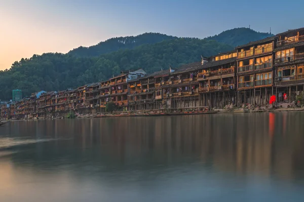 Traditional old wooden stilted houses on the banks of Tuo river, flowing through the centre of Feng huang Old Town on a calm quiet morning in summer, China