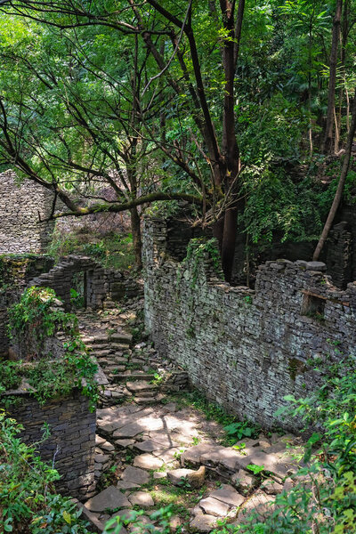 A pathway of concrete steps among old abandoned houses of an old village located in the middle of the lush tropical forest near Yangshuo, China