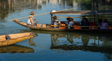 Feng Huang, Çin - Ağustos 2019: Geleneksel konik hasır şapka giyen Çinli adam, Tuo nehrinde turistleri taşıyan ve Fenghuang Eski Kasabası 'nın merkezinden geçen uzun, tahta bir teknede oturuyor.