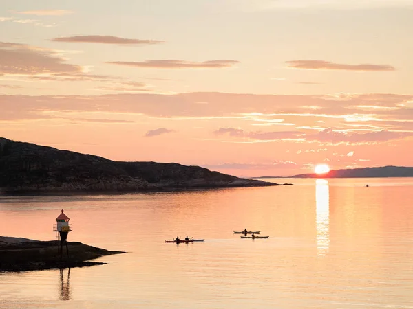 A lighthouse, three kayaks and a white sun, falling over the horizon, the sun in the red sunset in the Norwegian fjords on the Lofoten Islands in summer weather.