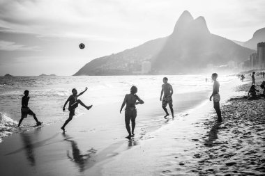 RIO DE JANEIRO, BRAZIL - FEBRUARY 24, 2015: A group of Brazilians playing on the shore of Ipanema Beach, with the famous Dois Irmaos mountain behind them clipart
