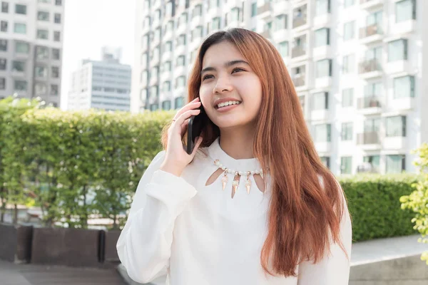 asian woman using smart phone on blurred background of residential building,Beautiful young woman with a smile while using smartphone