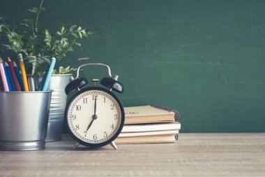 Sınıfta blackboard arka plan üzerinde ahşap masa çalar saat.