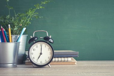 Sınıfta blackboard arka plan üzerinde ahşap masa çalar saat.