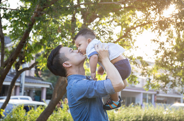 Father lifting son in hand and pretending to wheel with pleasure on blur background at garden 