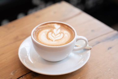 kafede ahşap masa üzerinde beyaz bir fincan kahve latte.