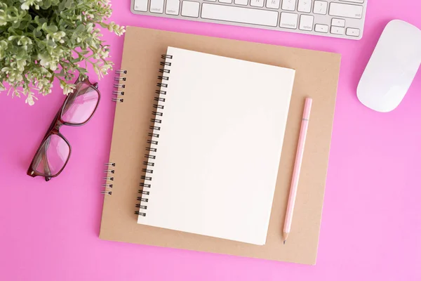 Blank notebook with keyboard and pencil on pink background