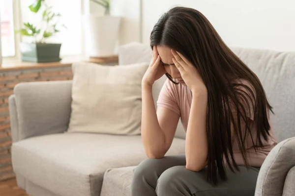 Asiatico donna sono holding loro mani a il testa in dolore su il divano a casa — Foto Stock