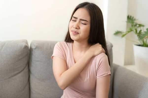 Asiatique fille avoir épaule douleur assis sur canapé à la maison . — Photo