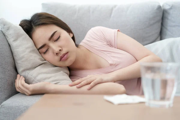 Malaise condition jeune fille asiatique dormir sur canapé après avoir vérifié la température et de prendre des médicaments et de l'eau — Photo