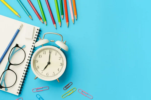 Flachbild-Foto vom Schreibtisch mit Buntstift, Büroklammer, Brille, Notizbuch, weißer Retro-Uhr, Draufsicht auf den Kopierraum — Stockfoto