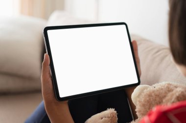 Asyalı küçük bir kızın elindeki boş dijital tablet, Tablet beyaz ekran. Evindeki kanepede otururken.