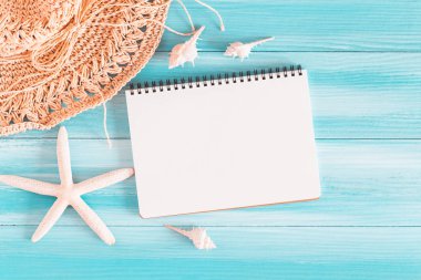Mavi ahşap masadaki boş defter, deniz kabukları ve mavi ahşap arka plandaki deniz yıldızı.