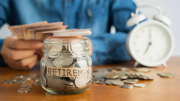 Een munt in een glazen fles afbeelding wazig achtergrond van zakelijke mensen zitten tellen geld en een retro witte wekker — Stockfoto