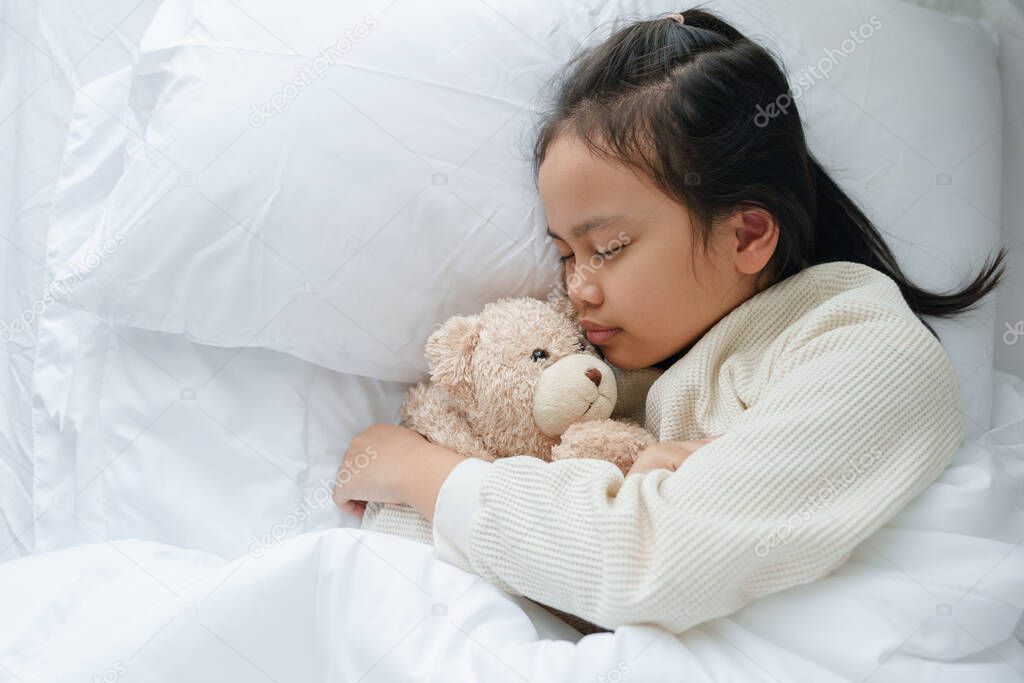Top view of Asian little girl sleeping and hug teddy bear in the bedroom