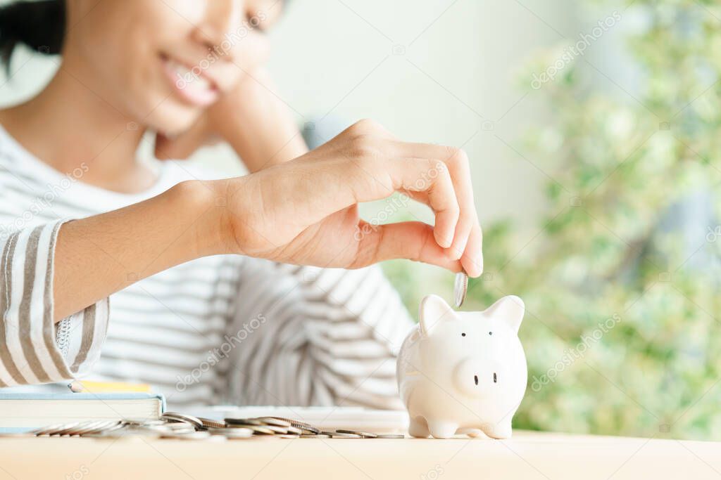  Hand of  Asian young girl are putting coins in a piggy bank at home, Close up of child happy smile, finance and saving money for future concept
