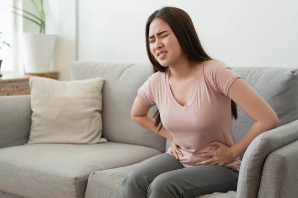 asian woman with menstruation and pain period cramps. young women having painful while sitting on sofa at her home