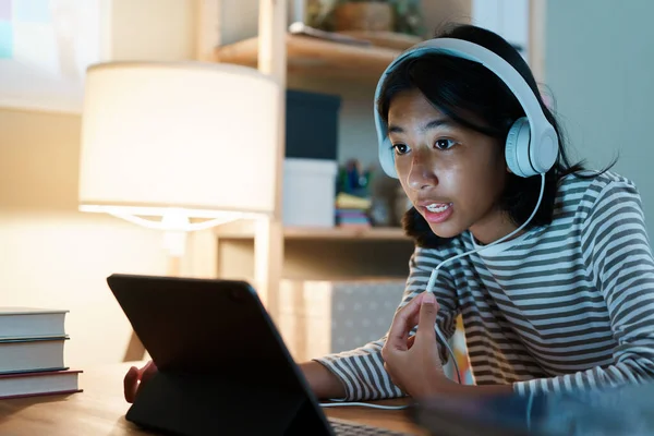 Asian girl study learning online via the internet on tablet with headphones on desk at night home. Concept online learning at home
