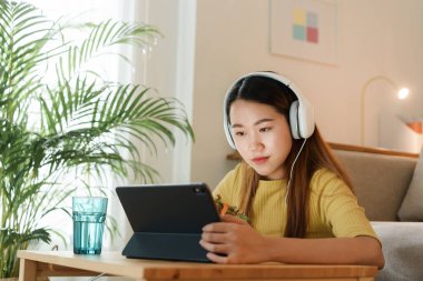 Güzel bir Asyalı genç kadın tablet kullanıyor ve öğle yemeğinde evde masa başında salata yiyor. konsept evden çalışıyor