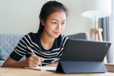 Ev ödevi. Öğrenci Asyalı kadın evde oturma odasında otururken tablet kullanıyor, evde online öğrenim kavramı