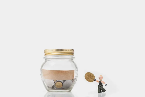 Yığın sikke para tasarrufu ile beyaz zemin üzerine kavanoz. Finansal yatırım gelecekte. Ukrayna bir sikke üzerinde 1 hryvnia yazıt. LEGO heykelcik yüzünde bir gülümseme ile bozuk para tutar.