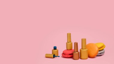 Altın ve bronz çivi jeli şişeleri ve pembe arka planda Fransız çok renkli badem kurabiyeleri. Manikür salonu için bira. Metnin için metin boşluğu. Polonya jeli. Manikür Pedikür