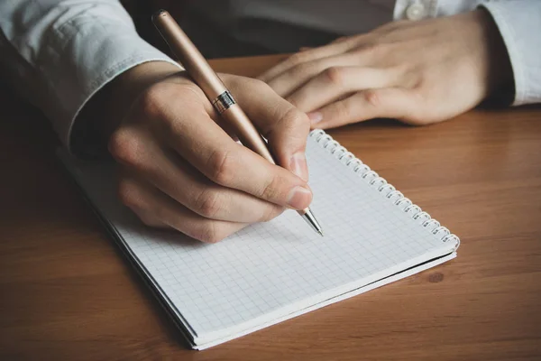 a man with a pen in his hand writes in a notebook close up