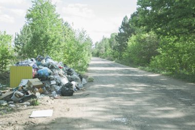 Güneşli bir günde ülkenin kum yolu yakınında yasadışı dökümü. Doğada çöp kirliliği. Ormanın yakınındaki kirli çöplük