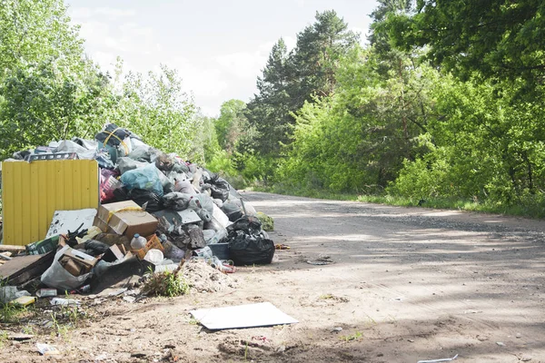 Despejo ilegal perto da estrada de areia do país no dia ensolarado. Poluição do lixo na natureza. Dirty dump perto de madeiras — Fotografia de Stock