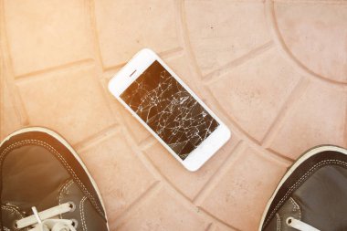 kırık akıllı telefon ekranı. Ayaklar ve kiremit zemin üzerinde kırık akıllı telefon. Üst görünüm kırık telefon 