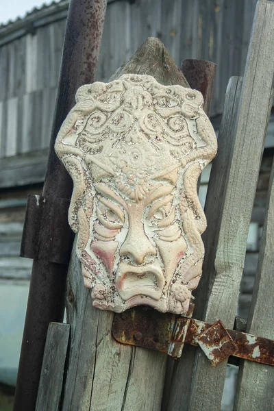 Old african ancient handmade mask on wooden fence near house. African culture traditional masks close up