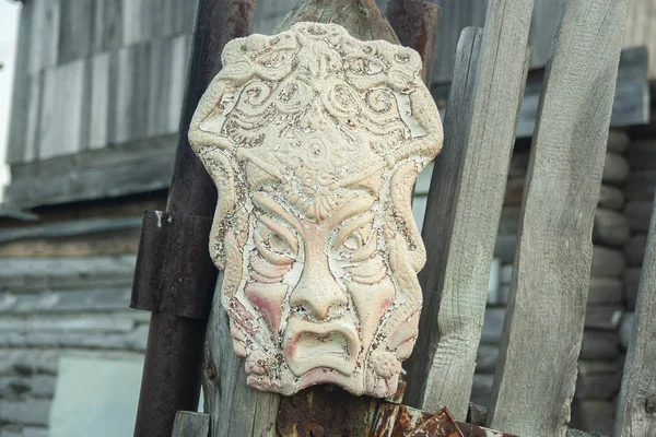 Old african ancient handmade mask on wooden fence near house. African culture traditional masks close up
