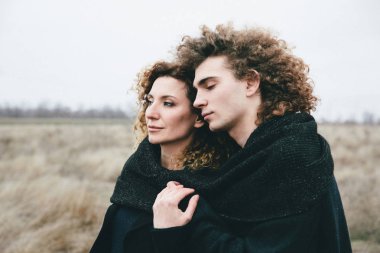 alan ve gökyüzü arka plan üzerinde Yetişkin oğlu ve kıvırcık saçlı anne sarılma