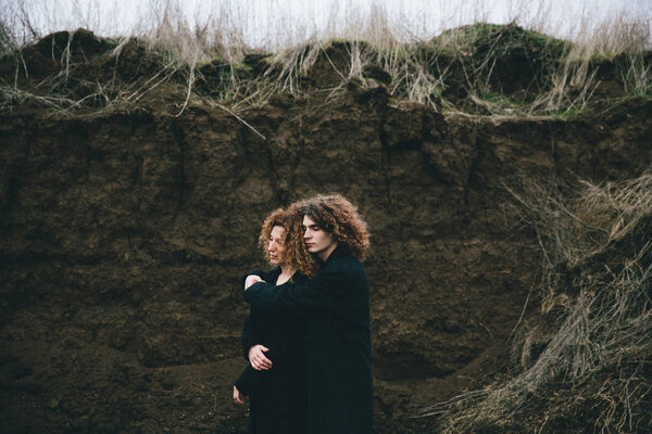 взрослые сын и мама с вьющимися волосами на фоне оврага
