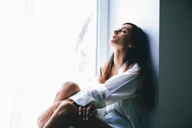 evde yatak odasında pencere üzerinde oturan genç kadın