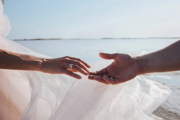ใกล้ชิดของคู่รักที่เพิ่งแต่งงานจับมือกันบนชายหาด ความรัก . — ภาพถ่ายสต็อก