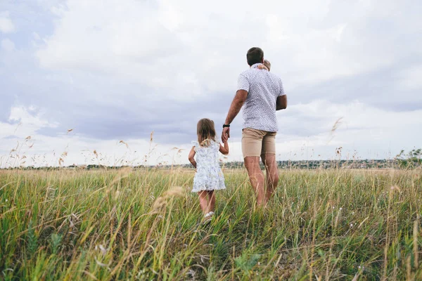 Schattig peuter knuffelen zijn vader en het houden van zijn nek en lopen zijn dochter — Stockfoto