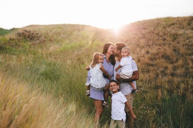 Happy dad and children hugging and having fun outdoors in a wheat field. Sunset clipart