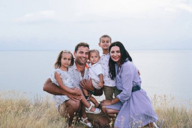Mutlu ebeveynler ve çocuklar bir buğday tarlası ve nehir görünümünde açık havada eğlenmek.