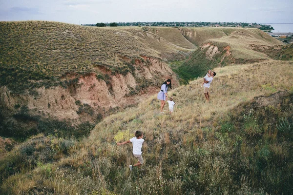Genitori felici e bambini stanno camminando all'aperto in un campo di grano e vista sulle colline. Vista posteriore — Foto Stock