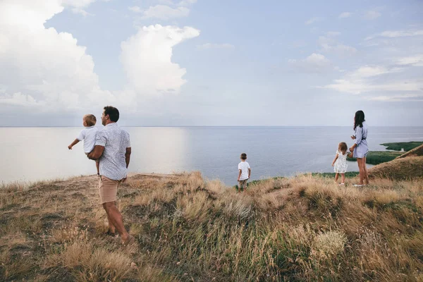 Padres felices y niños están mirando en dirección a un río al aire libre en un campo de trigo y vista al río . —  Fotos de Stock