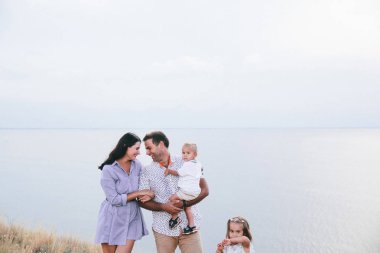 Mutlu ebeveynler birbirlerine bakıyorlar ve çocuklar buğday tarlası ve nehir manzarasıiçinde dışarıda eğleniyorlar..