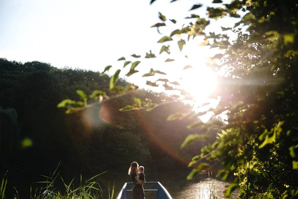 Вид спереду мати і син обіймає міст на озері в літній вечірній час — стокове фото