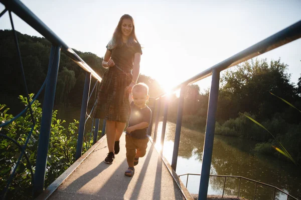 Mutter und kleiner Sohn spazieren im Sommer abends auf der Brücke über den See — Stockfoto